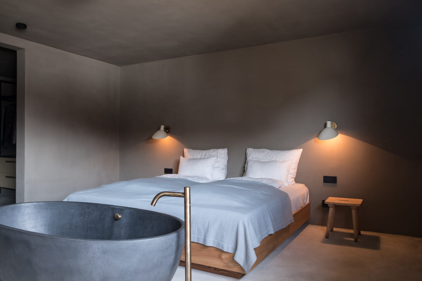 Modern bedroom featuring a double bed with white linens, a concrete bathtub, and minimalist decor.