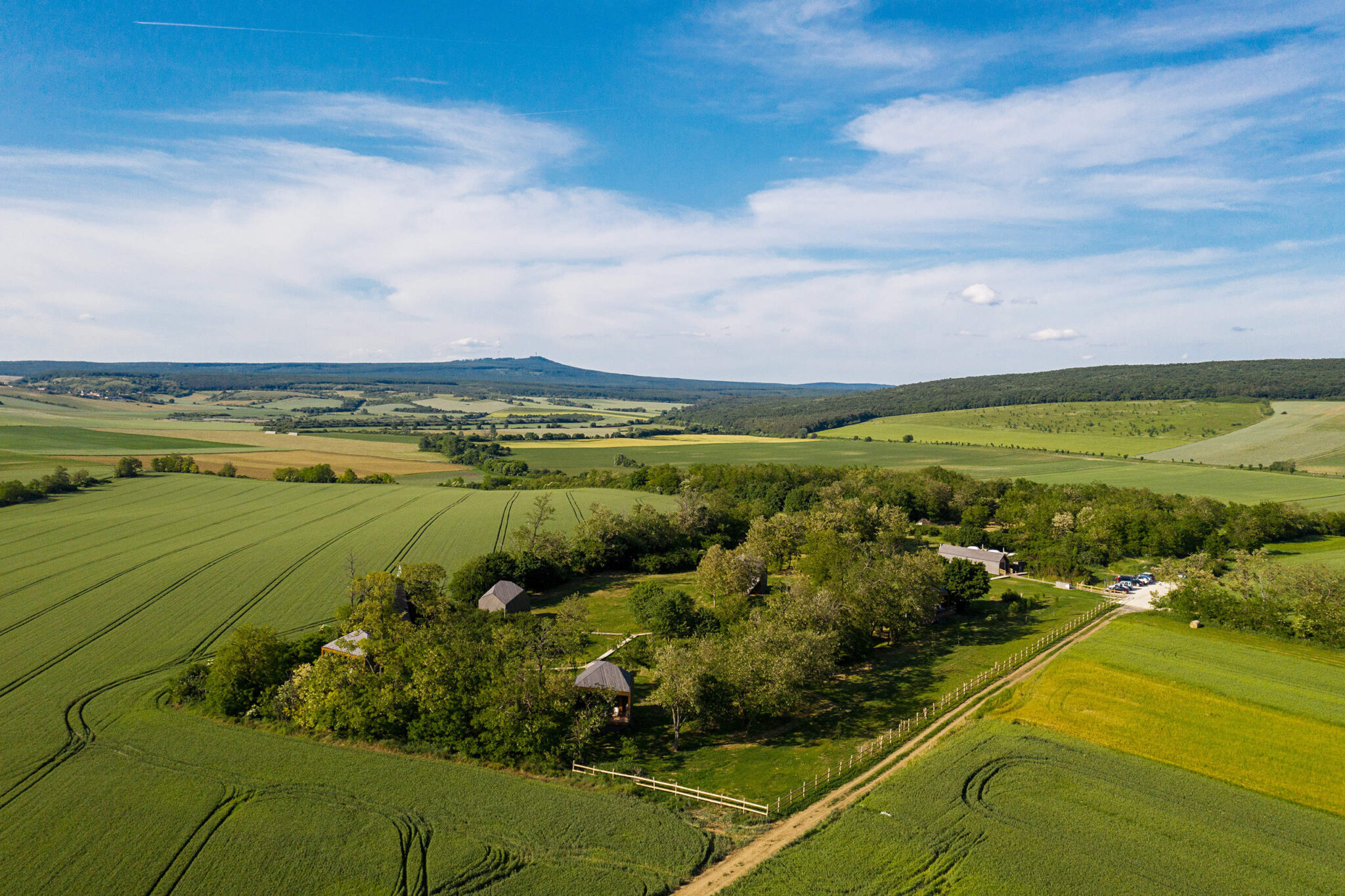 Aerial view of Rock Cabins resort surrounded by lush green fields and distant hills under a blue sky.