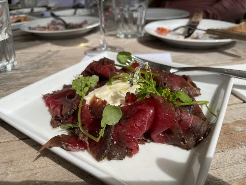 Plated dish of cured meat garnished with herbs and a dollop of cream, set on a wooden table.