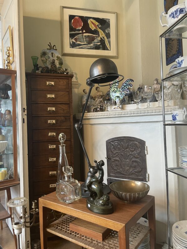 Antique lamp and decor on a wooden table, with a wooden cabinet and various glassware in the background.