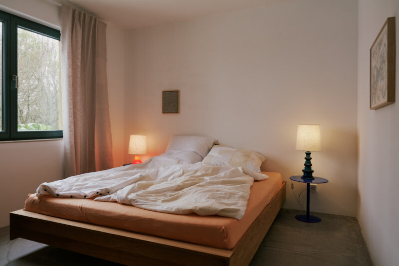 Cozy bedroom with a large bed, white bedding, two bedside lamps, and a window with sheer curtains.