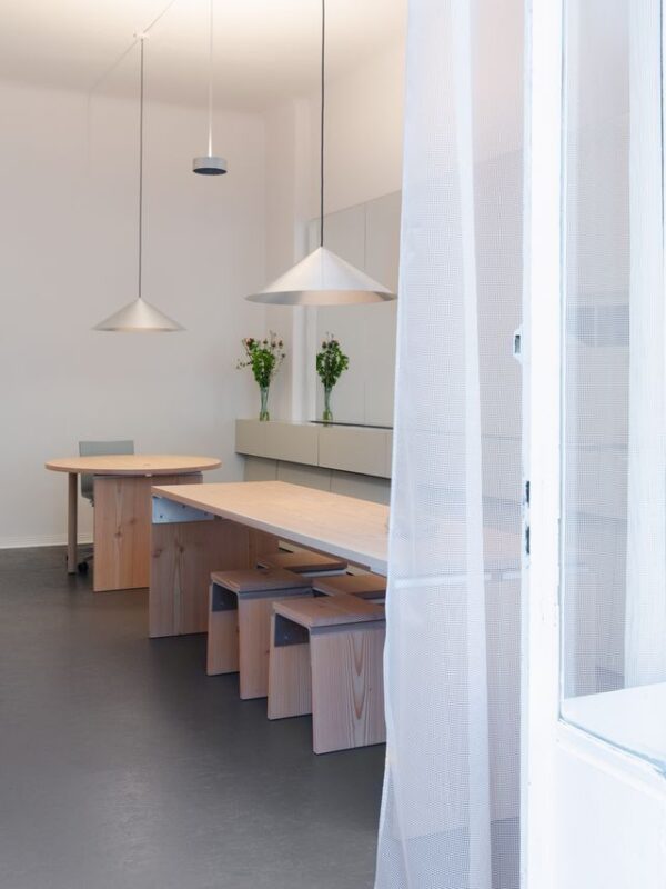 Modern dining area with a round wooden table, minimalist benches, and pendant lights, featuring floral arrangements.
