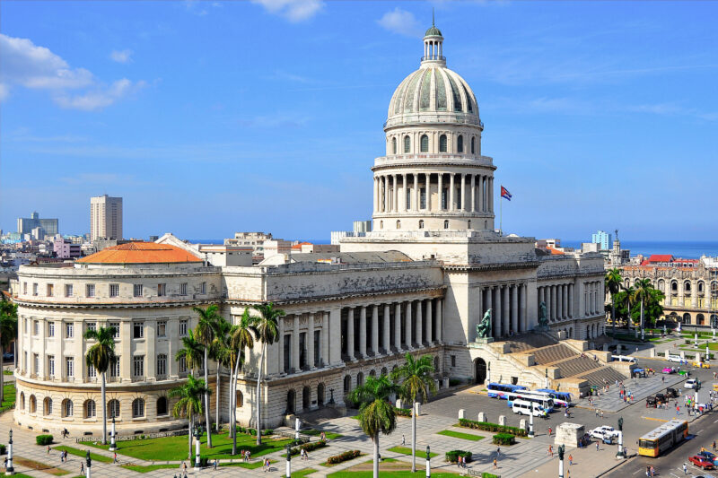 Havana's Capitolio building with a dome, surrounded by palm trees and cityscape under a clear blue sky.