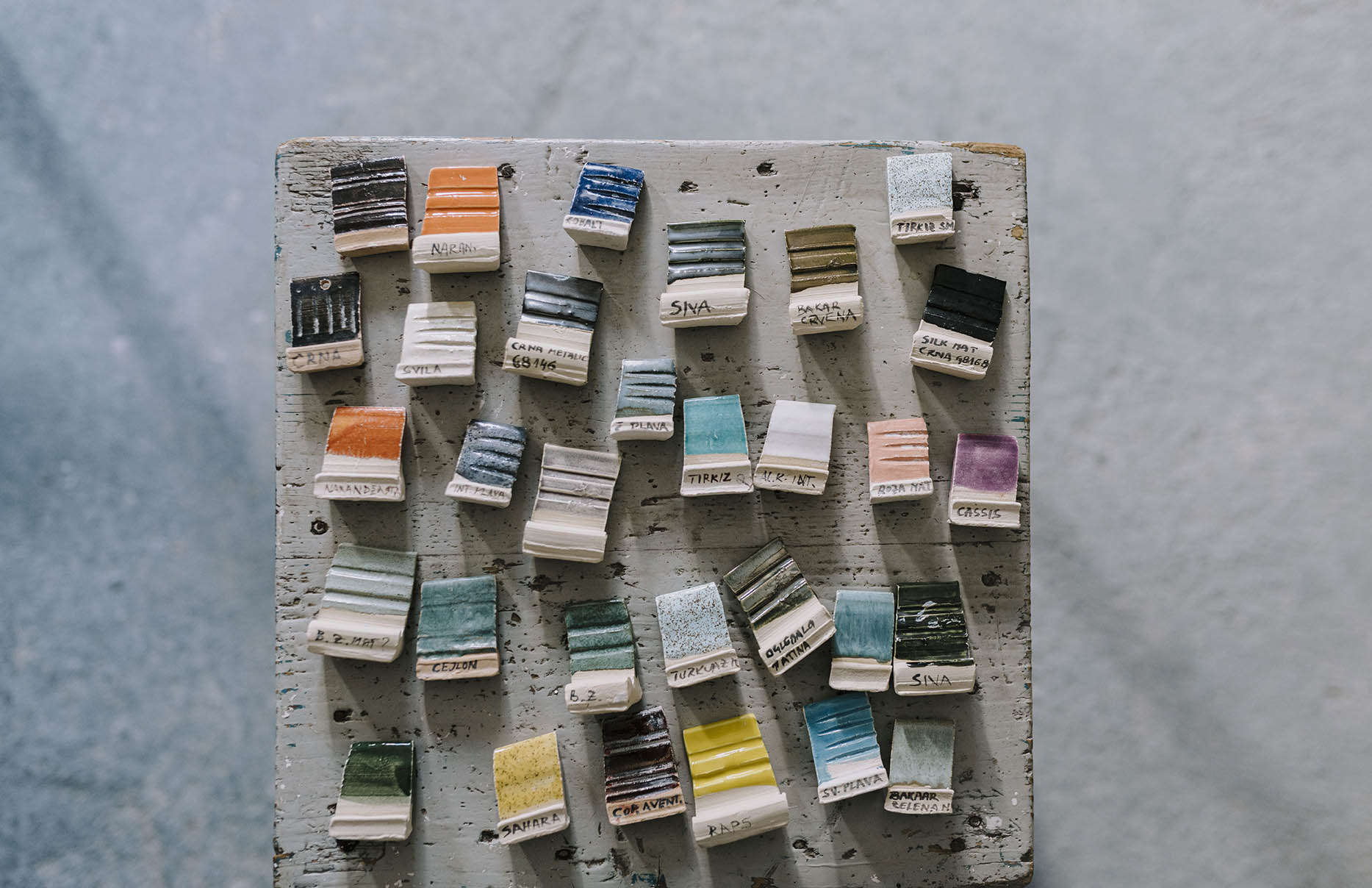 Color swatches arranged on a wooden table, showcasing various shades and textures, labeled with names and codes.