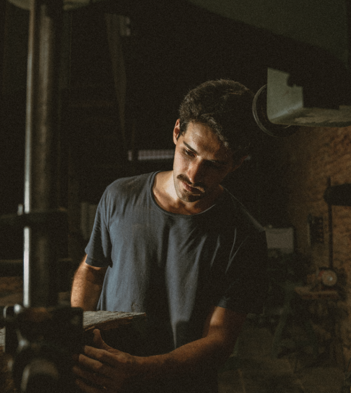 Man working with wood in a workshop, focused on a piece being cut by a machine.