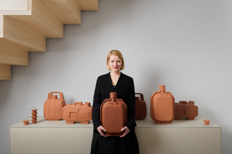Johanna Seelemann poses with terracotta containers against a minimalist backdrop, showcasing her artistic work.