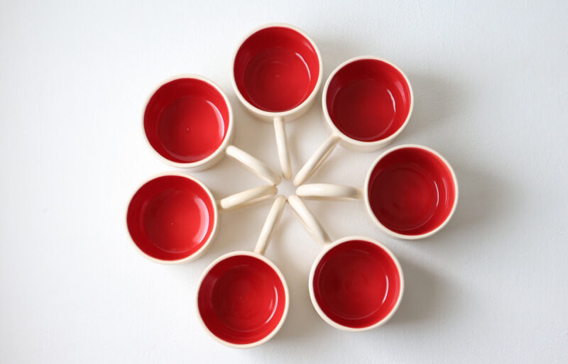 Seven small cups with red interiors arranged in a circular pattern on a white background.