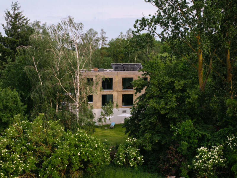 Modern building with large windows, surrounded by lush greenery and trees, set in a natural landscape.