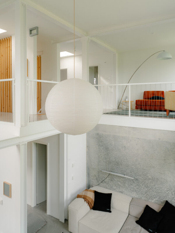 Modern interior of Palais Brut featuring a large round pendant light, a sofa, and an orange chair in a bright space.