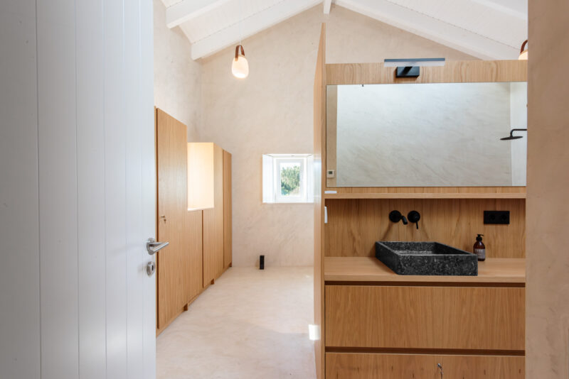Modern bathroom with wooden cabinetry, a dark stone sink, and a large mirror, featuring a bright, airy atmosphere.