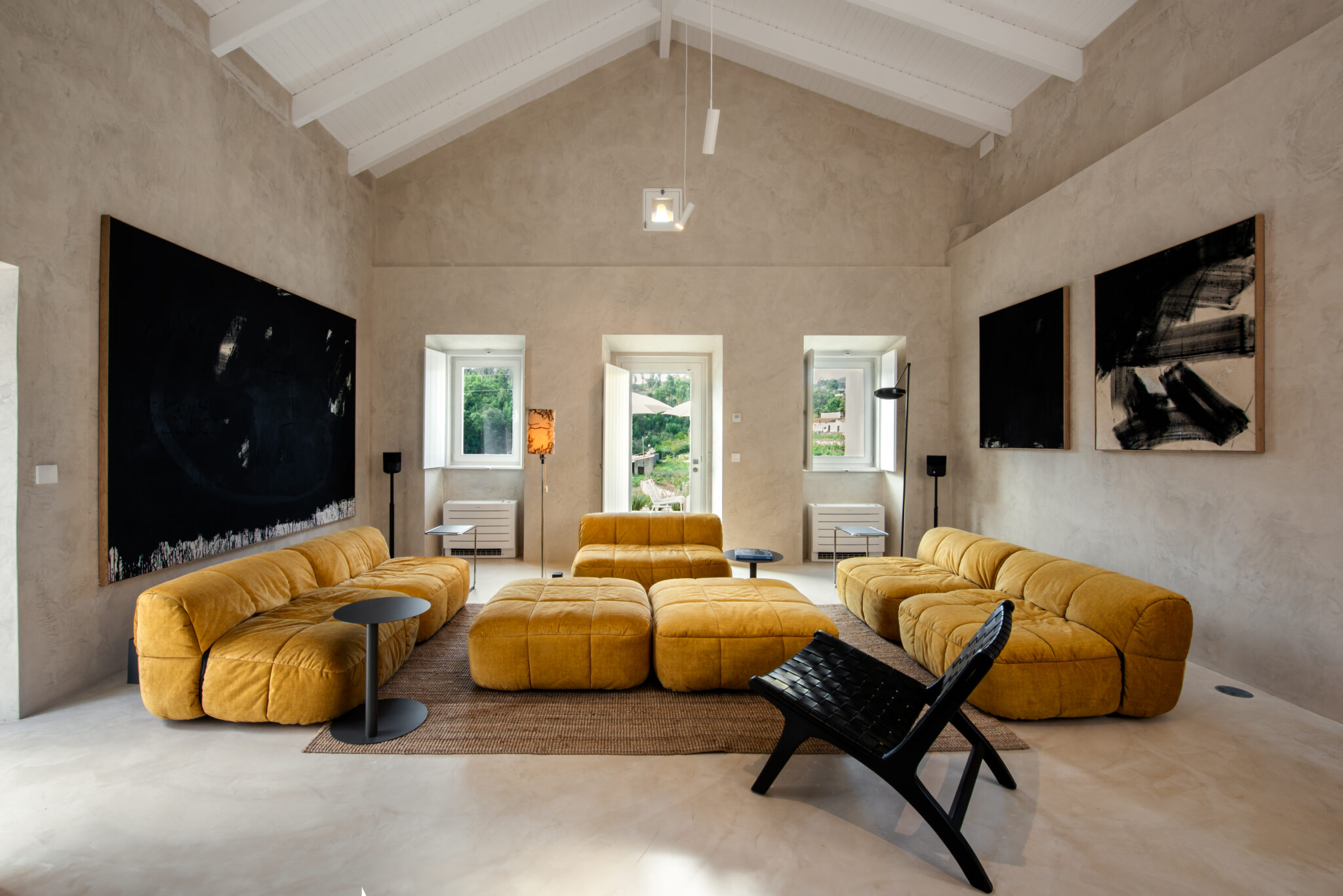 Modern living room featuring a yellow sectional sofa, black chairs, and large abstract art pieces on textured walls.