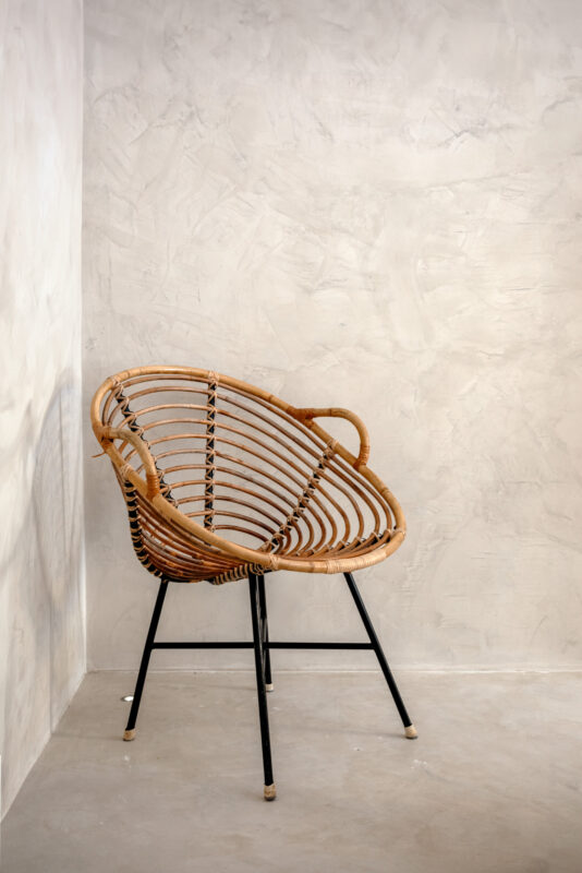 Rattan chair with a curved design, resting against a textured gray wall in a minimalist setting.