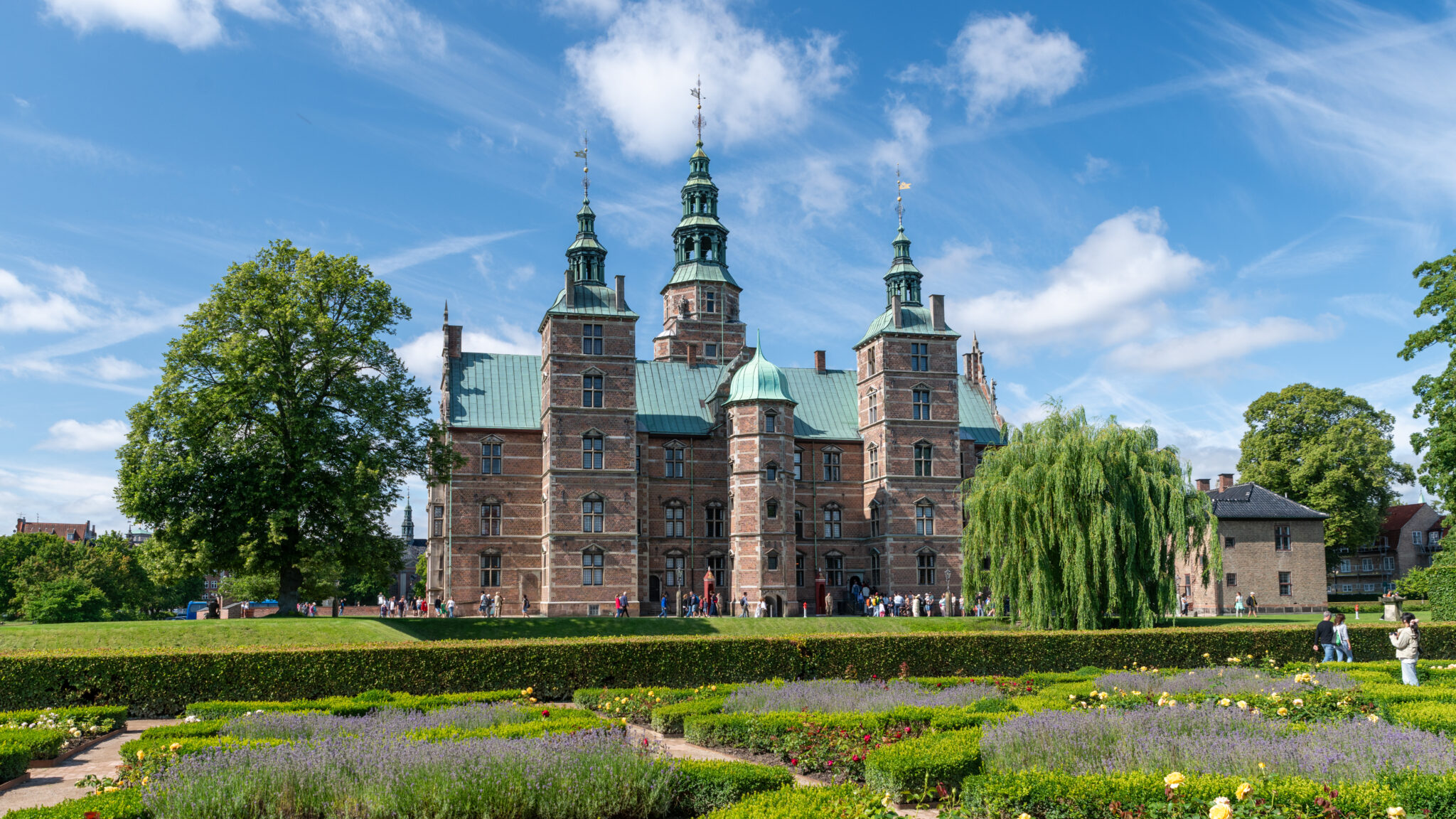 Rosenborg Castle in Copenhagen, Denmark, surrounded by gardens and visitors under a blue sky.