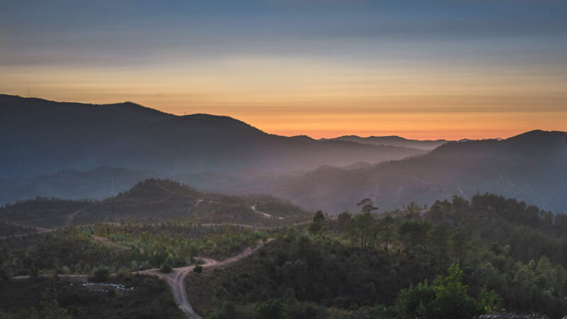 Distant view of Serra de Monchique at sunset, with layered mountains and a winding road through the landscape.