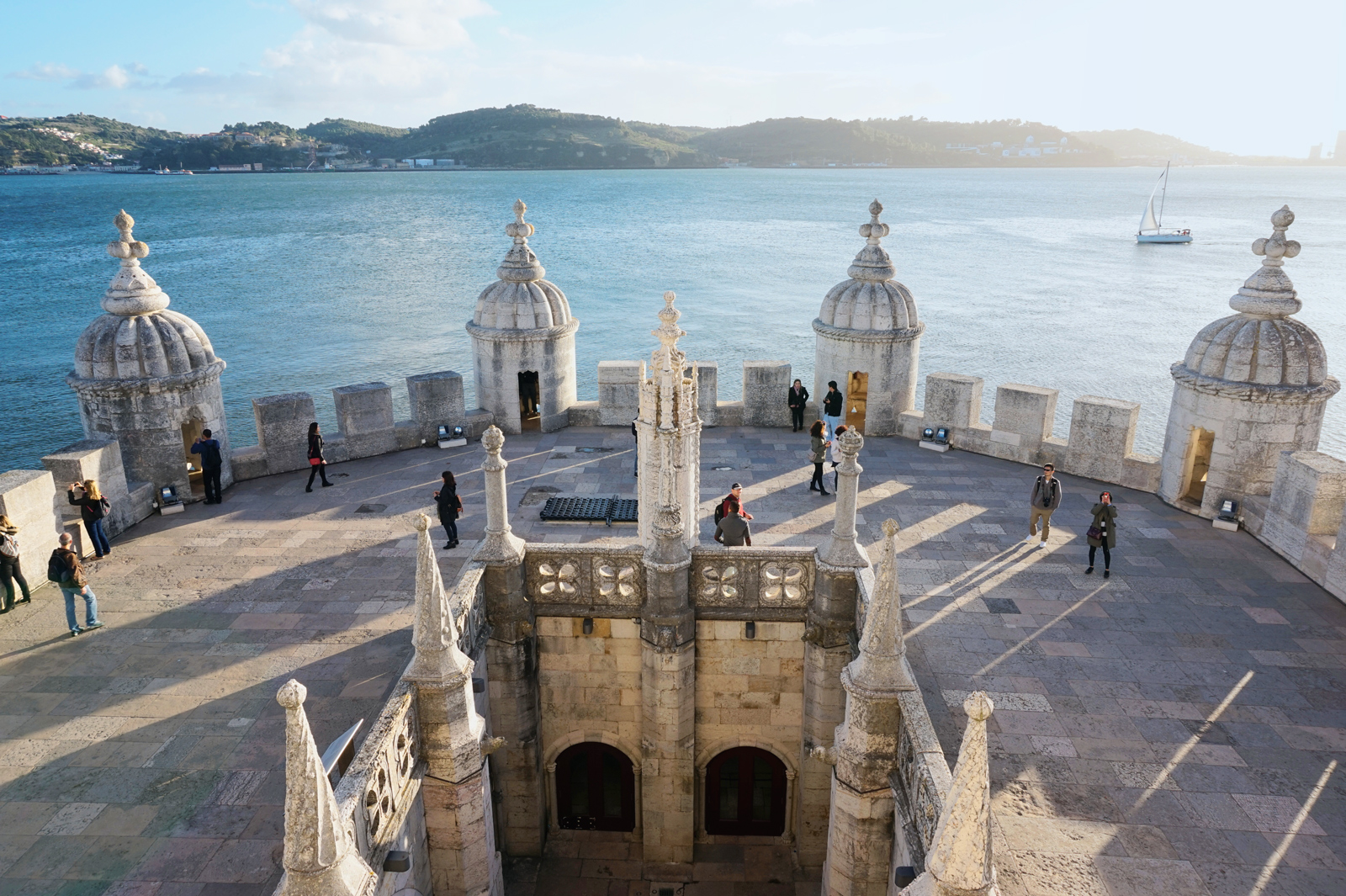 View from the top of Belém Tower in Lisbon, showing ornate stone turrets and visitors against a backdrop of the river.