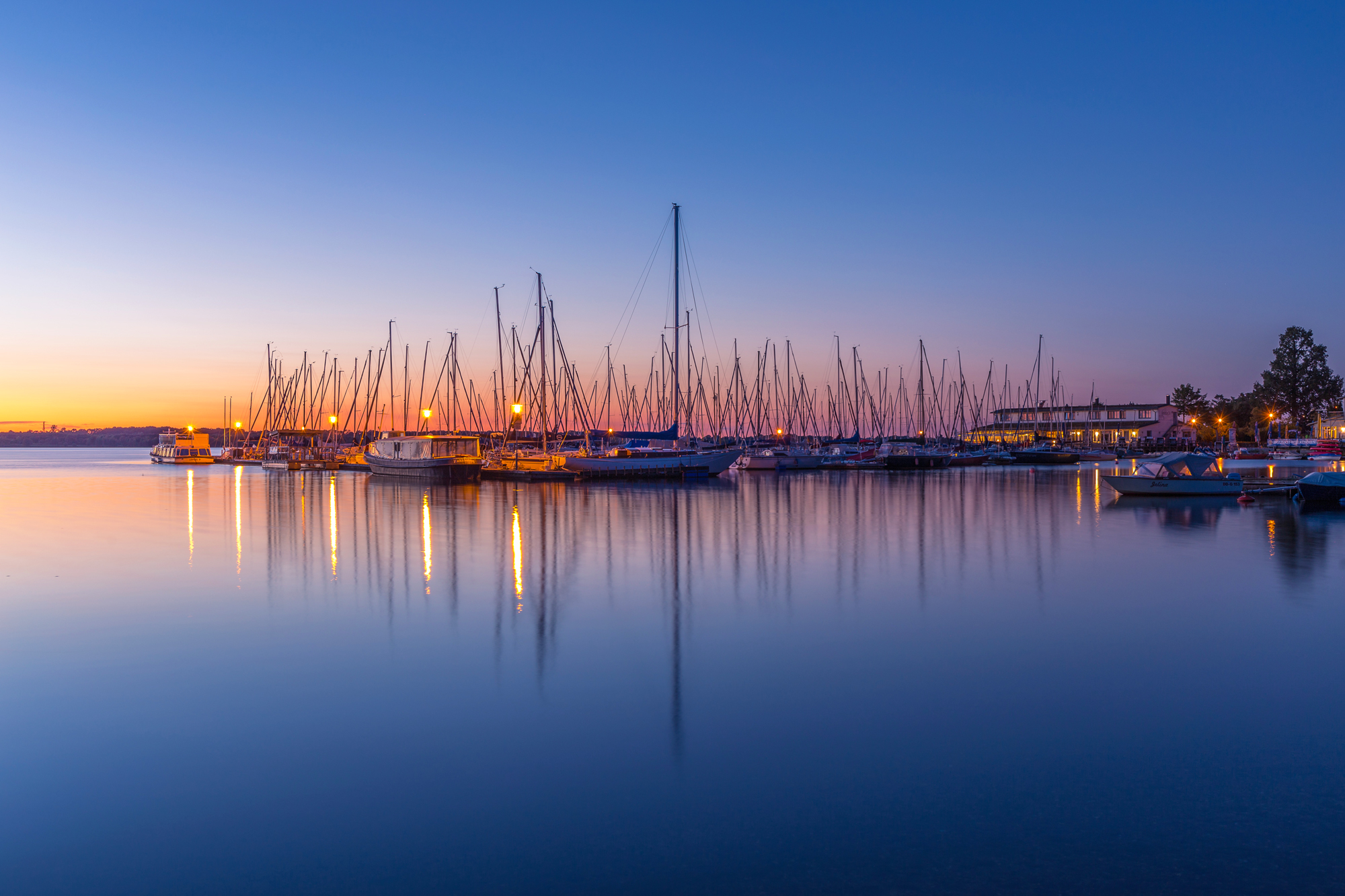 Serene sunset over Zöbigker Hafen at Cospudener See, with sailboats reflecting on calm water.