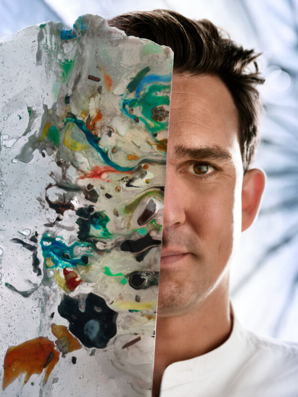 Thijs Biersteker holds a translucent, colorful art piece, partially obscuring his face, with a blurred background.