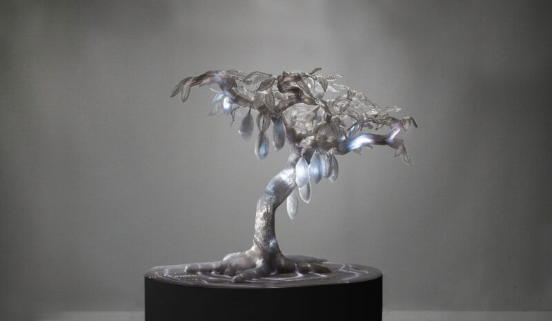 Sculpture of a stylized tree with translucent leaves and integrated lighting, displayed on a dark pedestal.