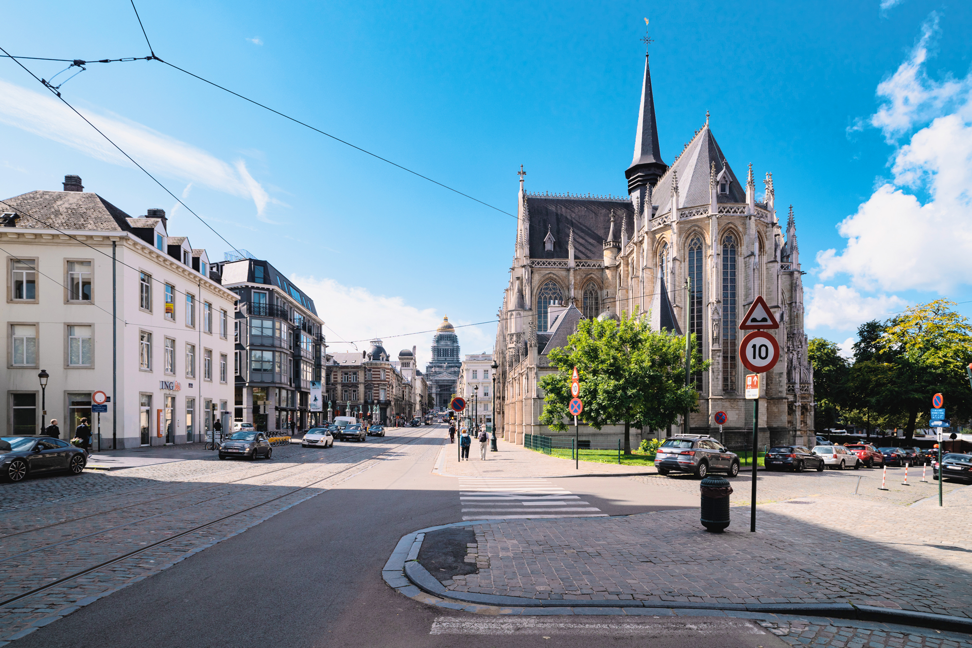 Church of Our Blessed Lady of the Sablon in Brussels, with a clear blue sky and street view featuring cars and buildings.