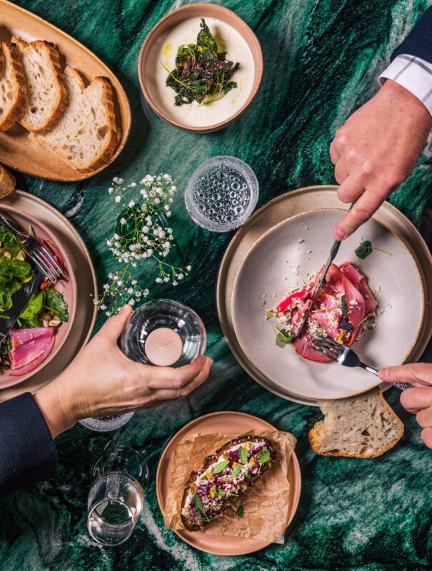 Elegant table setting featuring gourmet dishes, fresh greens, and bread on a green marble surface.