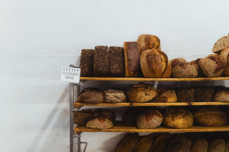Shelves filled with various types of bread, including loaves and rolls, with a sign labeled "YESTERDAY'S BREAD.