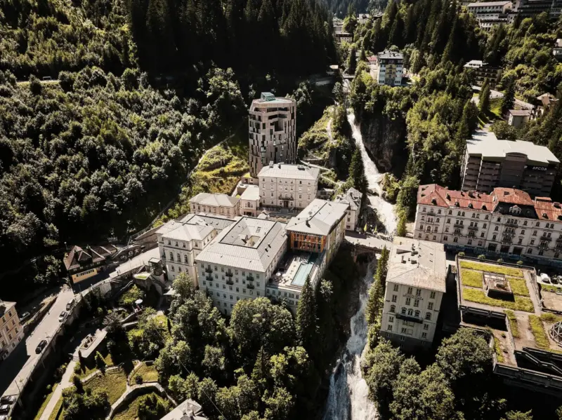 Aerial view of Badeschloss hotel complex surrounded by lush greenery and a river, showcasing modern architecture.
