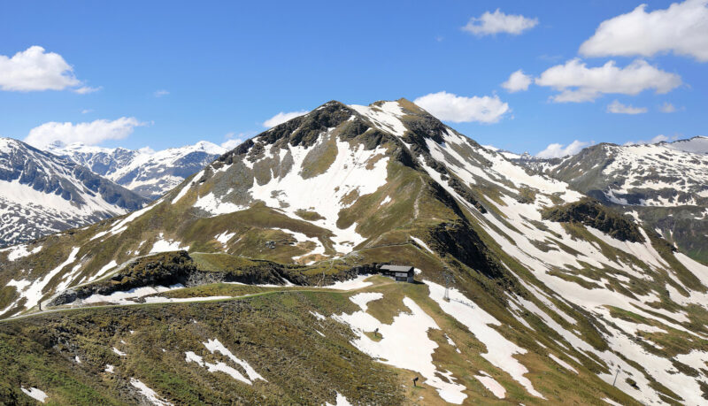 Snow-capped mountains and green hills under a blue sky, viewed from Stubnerkogel towards the southwest.