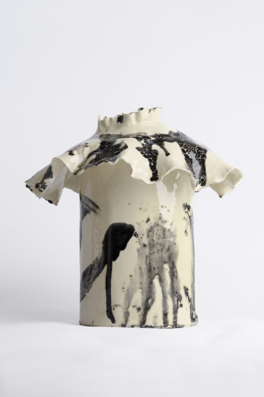 Detail of a ceramic vase with a ruffled edge, featuring a glossy white surface with black paint splatters.