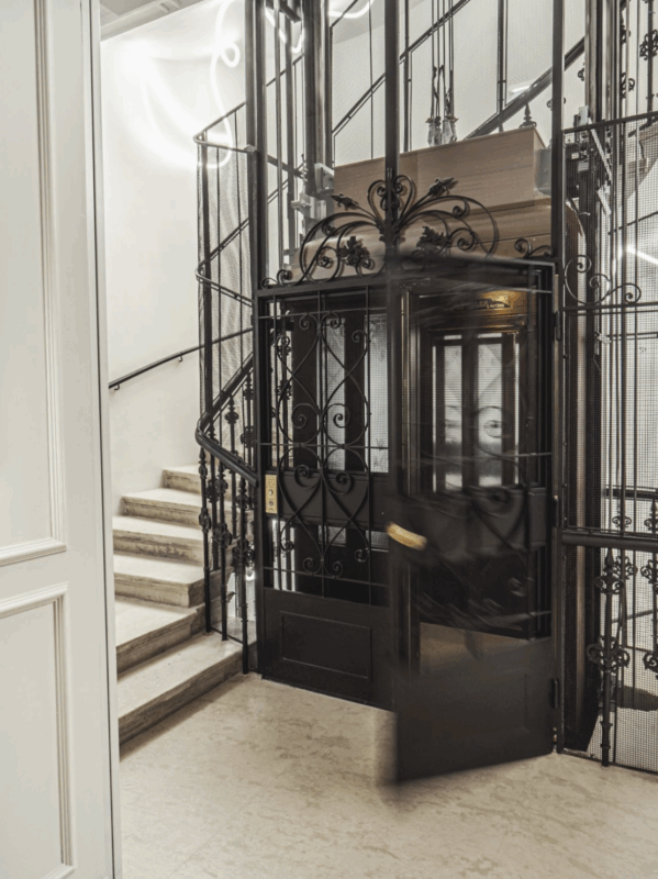 Elegant black elevator doors open in a staircase area with ornate railings and a modern design.