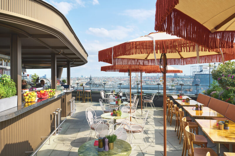Rooftop terrace of Hotel Motto with colorful umbrellas, tables, and a view of the city skyline.