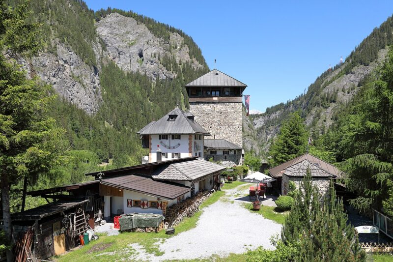 Historic Burg Klammstein castle surrounded by mountains and greenery, with a clear blue sky above.