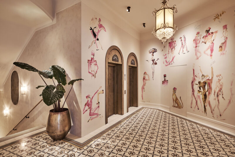 Stylish hotel lobby featuring artistic wall murals, elegant lighting, and patterned tile flooring.