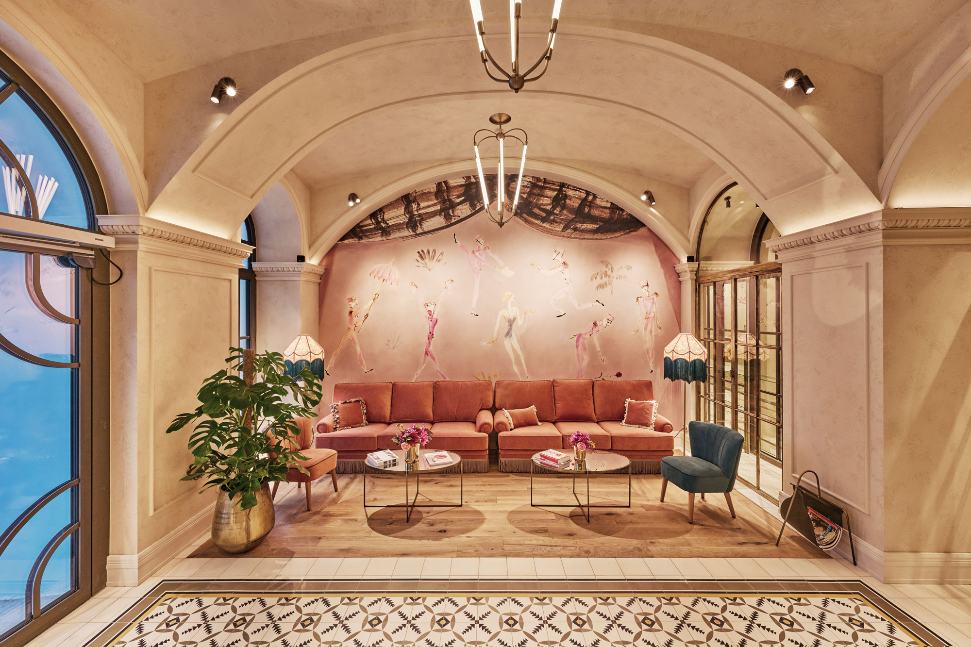 Elegant hotel lobby featuring a pink sofa, decorative tables, and a vibrant mural of dancers on the wall.