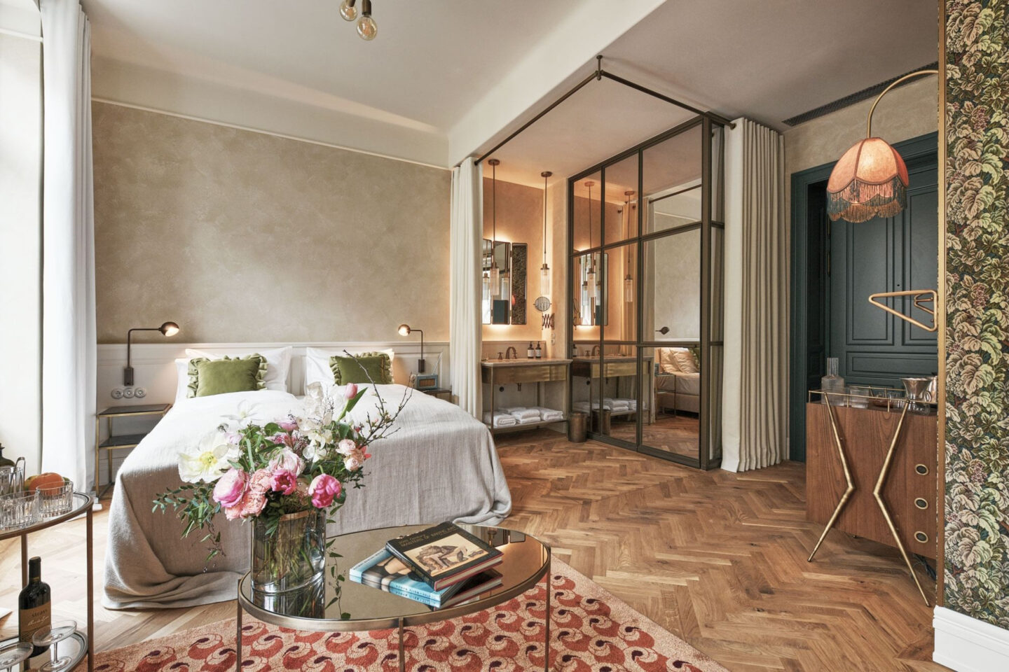 Deluxe hotel room featuring a double bed, stylish decor, a glass partition, and a floral arrangement on a coffee table.