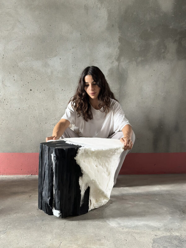 Woman in a white shirt sits on the floor, examining a large black and white sculptural piece against a gray wall.