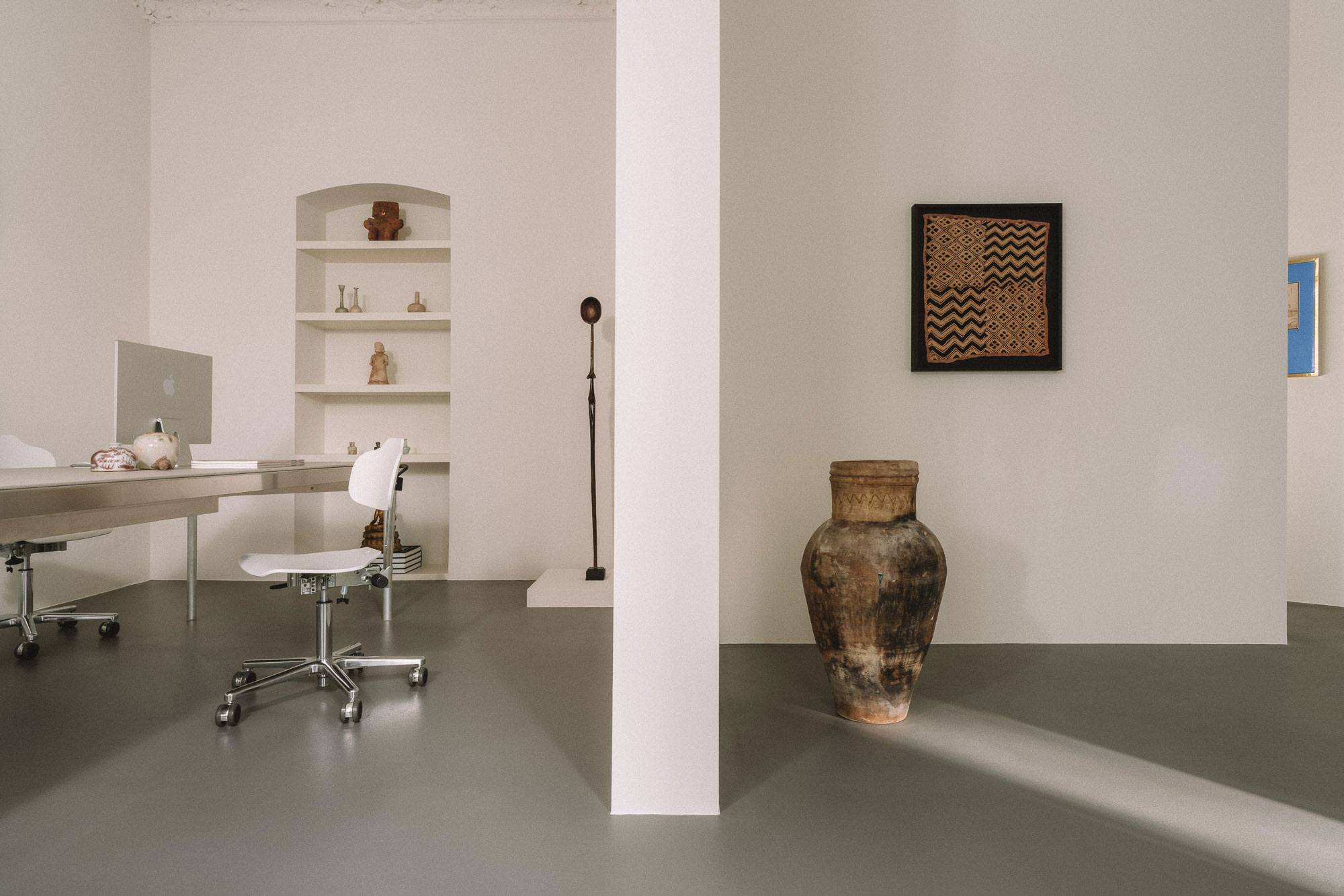 Minimalist interior featuring a workspace with a computer, a large vase, and art on the walls.