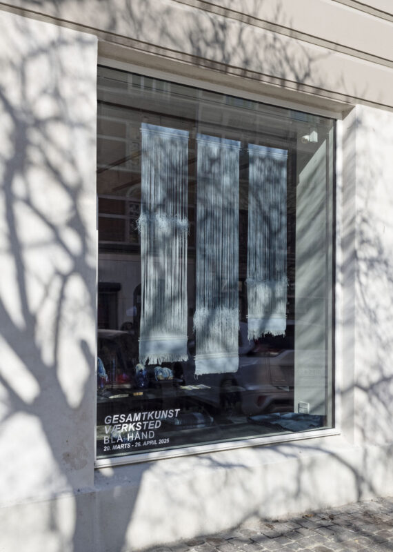 Art installation featuring three vertical panels with textured white patterns displayed in a gallery window, framed by tre...