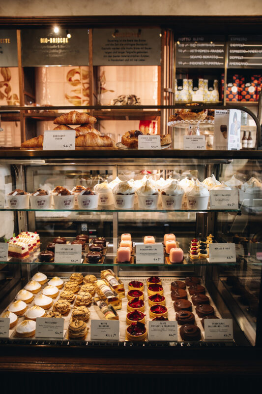Display case filled with various pastries and desserts, including croissants, cakes, and tarts, at Hotel Motto.