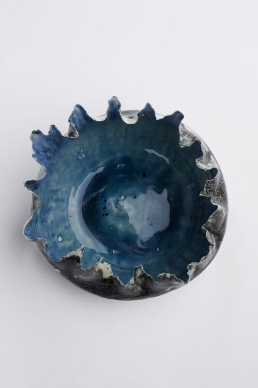 Ceramic bowl with a wavy edge, featuring a deep blue interior and a textured black exterior.