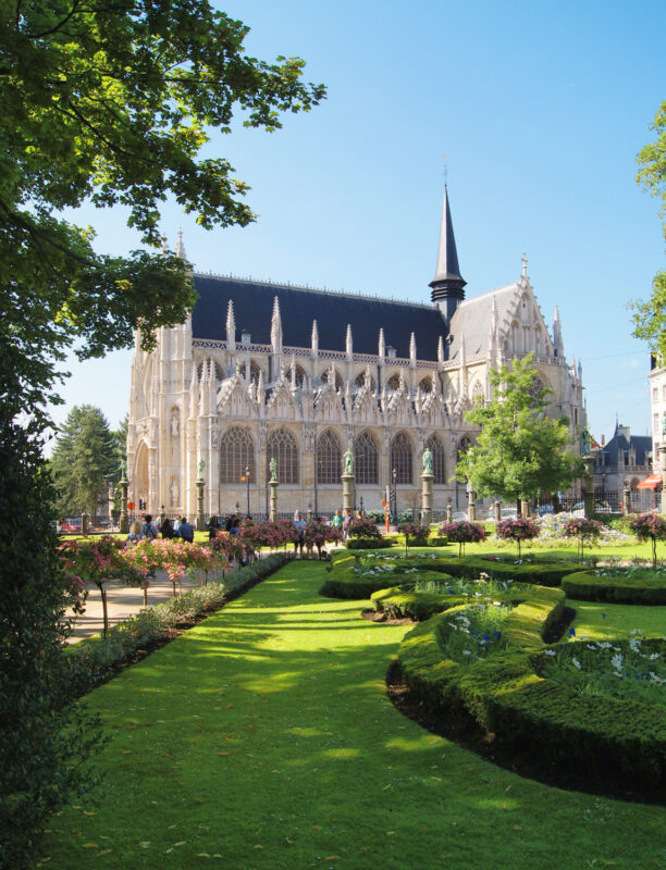 Gothic-style Notre Dame du Sablon church surrounded by manicured gardens and blue sky.