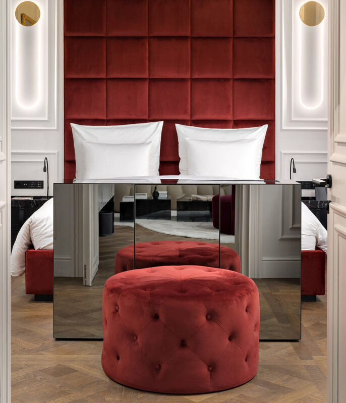 Luxurious hotel room featuring a red velvet headboard, mirrored furniture, and a chandelier, creating an elegant ambiance.