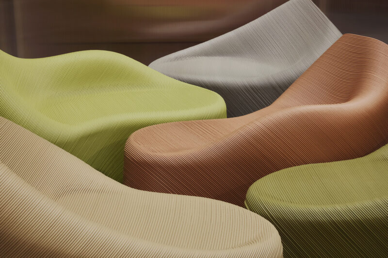 Colorful, curvy lounge chairs in green, beige, and brown, featuring a textured design, arranged artistically.