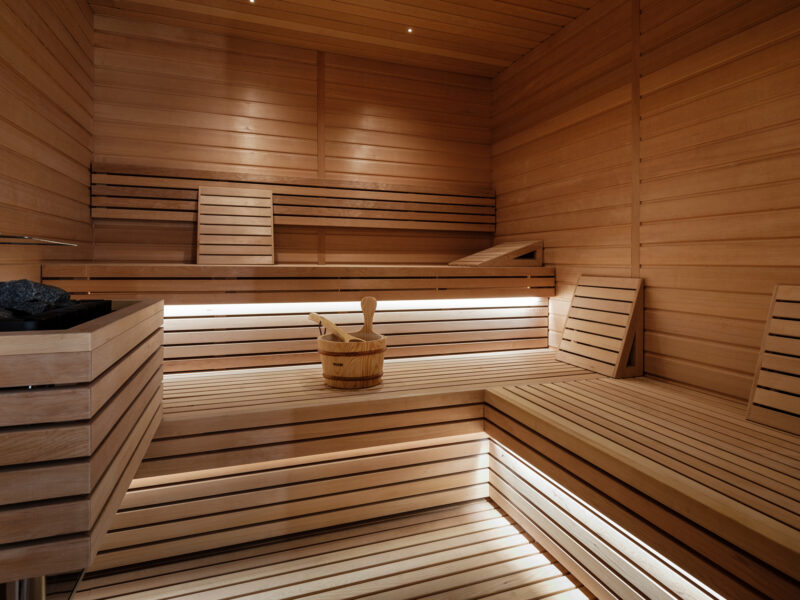 Wooden sauna interior with benches, a wooden bucket, and soft lighting, creating a warm and inviting atmosphere.