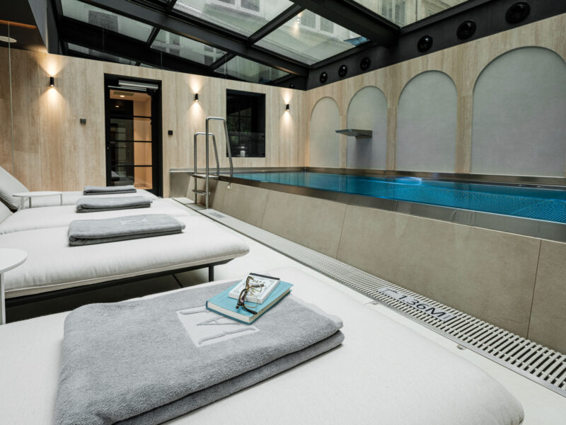 Indoor spa area featuring a pool, lounge chairs with towels, and a modern design with large windows.