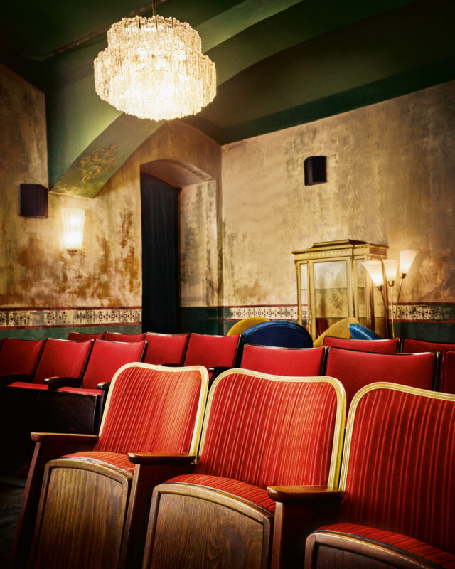 Empty red theater seats with a vintage chandelier and decorative walls, creating a nostalgic atmosphere.