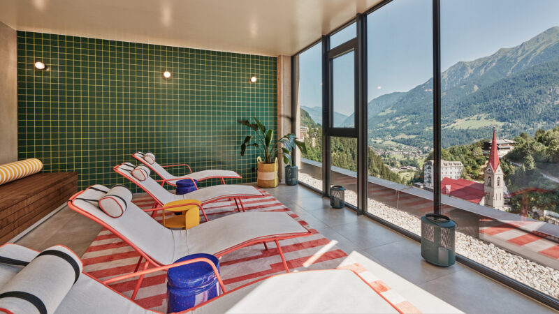 Relaxation area with lounge chairs, green tiled wall, large windows showcasing mountain views, and a cozy atmosphere.