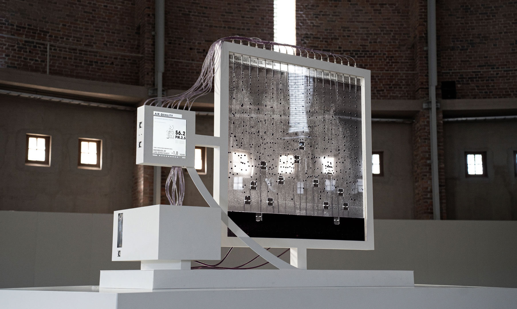 Art installation featuring a large, transparent panel with flowing liquid and digital displays, set in a spacious gallery.