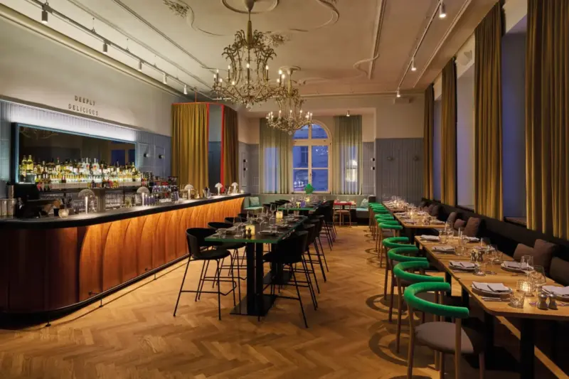 Elegant restaurant interior featuring a bar, tables with green chairs, and a chandelier in Bad Gastein.