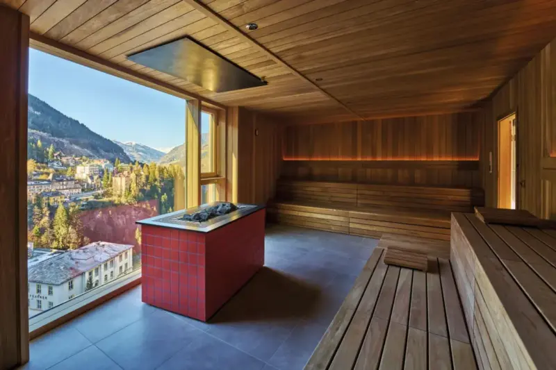Interior view of a sauna with wooden benches and a panoramic window showcasing a mountain landscape in Bad Gastein.