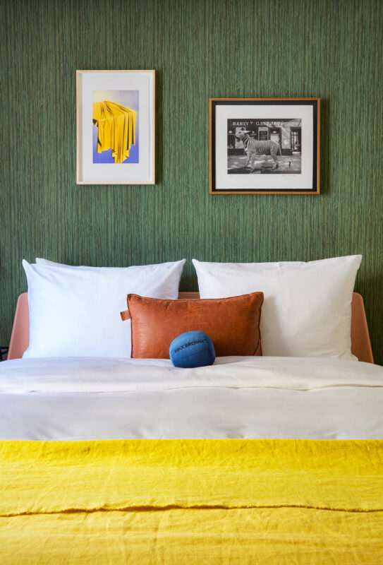 Bed with white pillows and a yellow blanket, featuring framed art on a green textured wall.